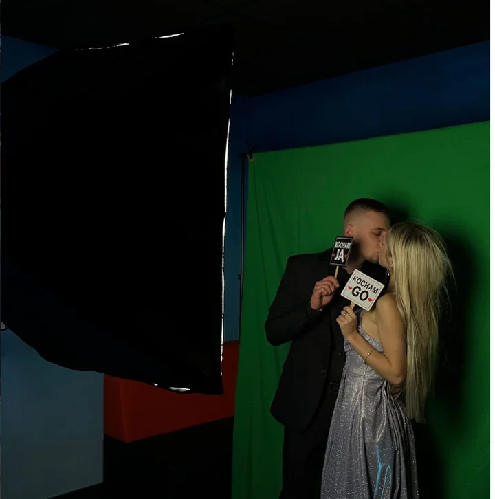 Para z rekwizytami pozuje przy fotobudce na tle fotograficznym